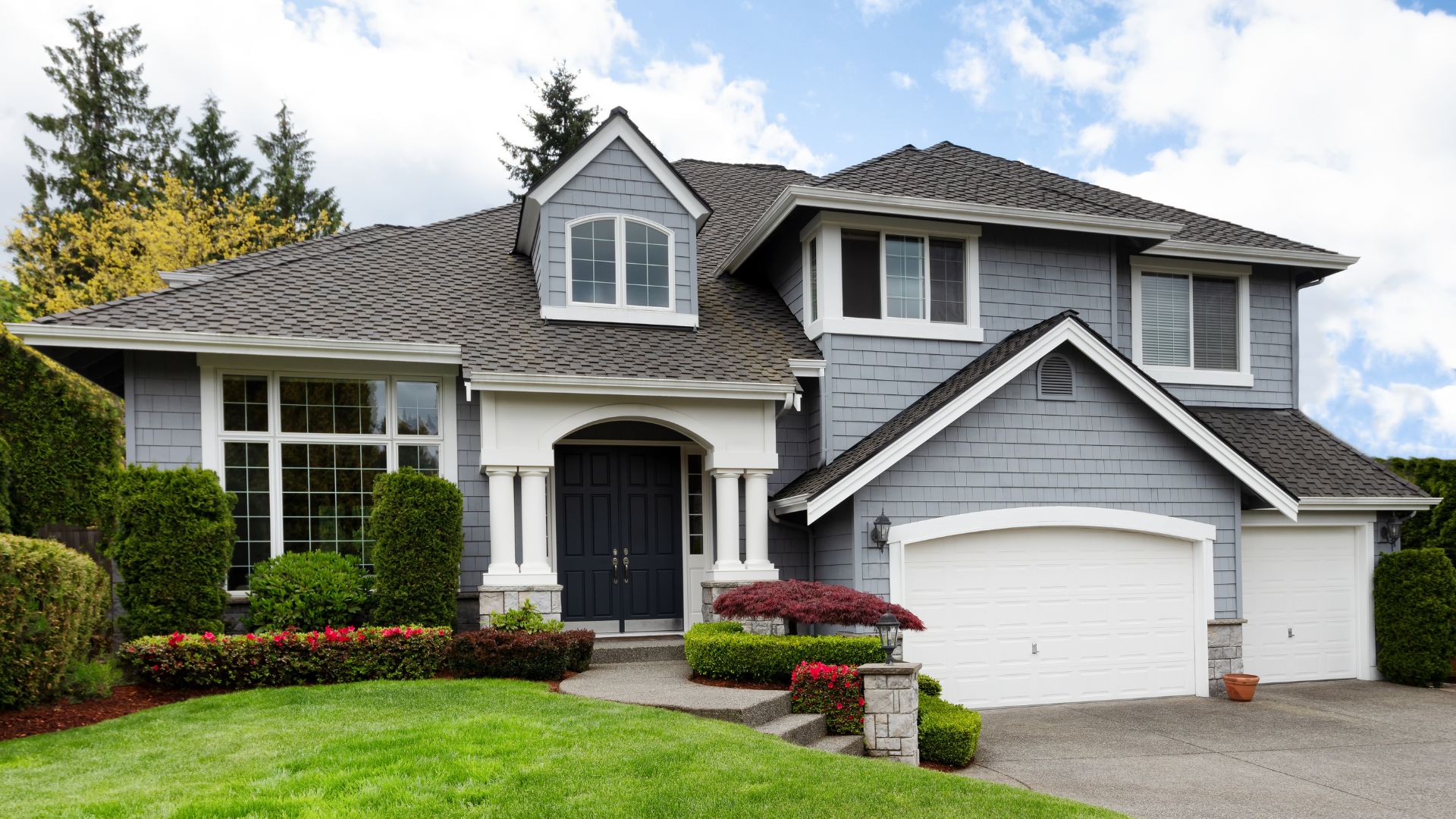 Gray two-story house with white trim, black door, and manicured landscaping