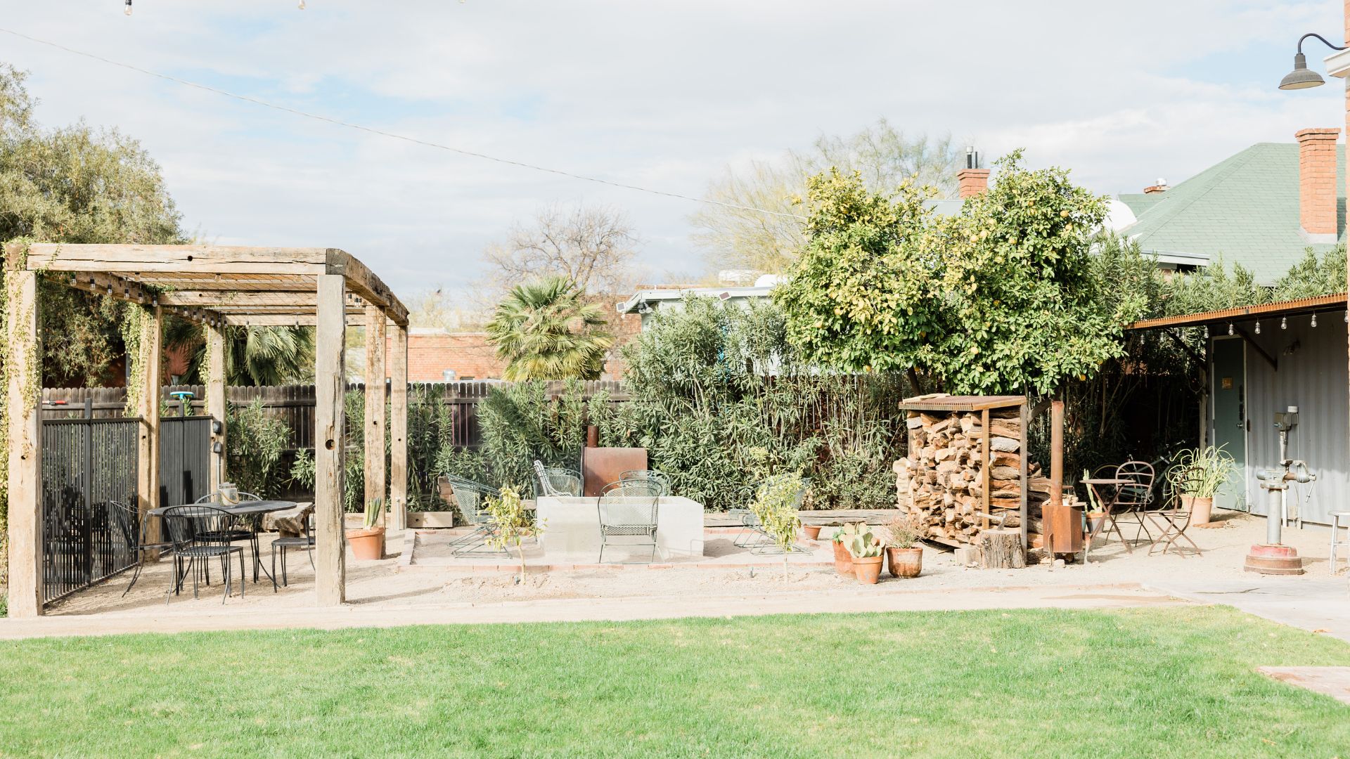 Backyard patio with wooden pergola, seating area, and neatly stacked firewood
