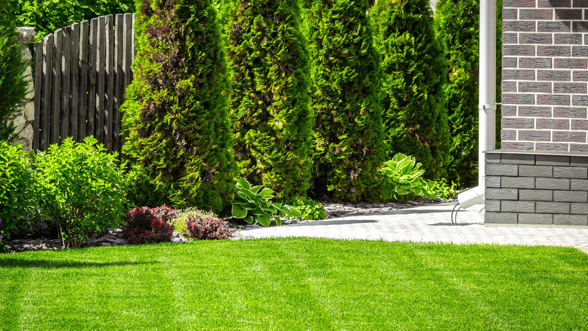 Manicured lawn with green shrubs, trees, and brick house background